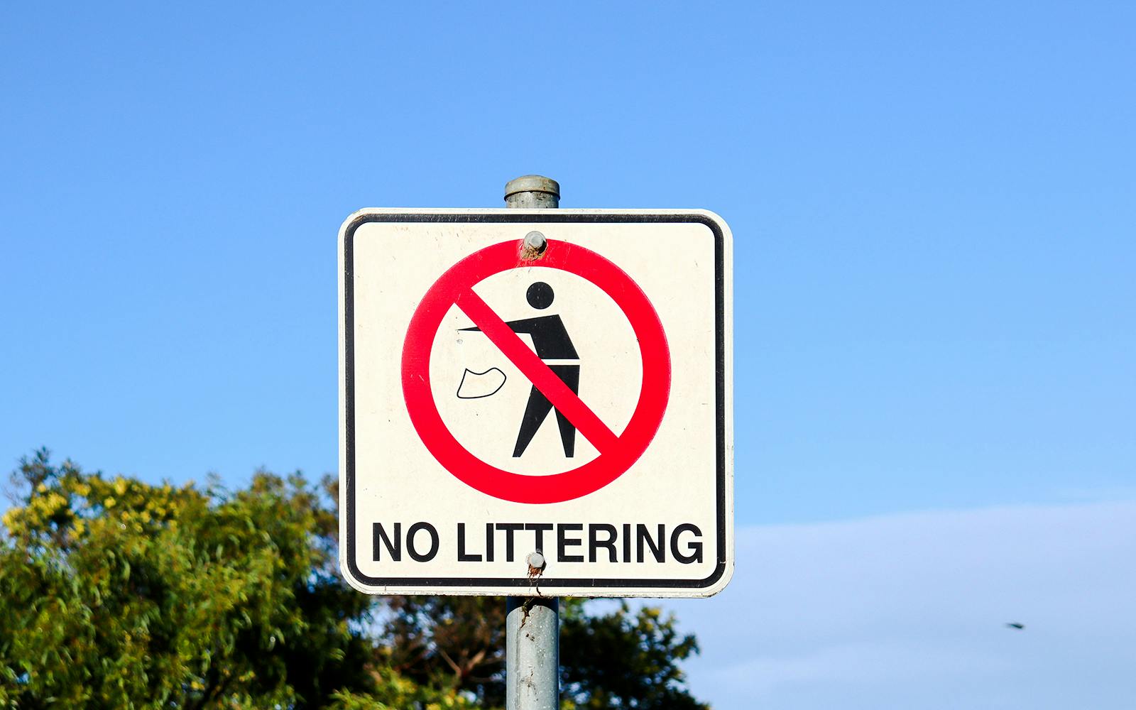 No littering sign with a red circle and slash over a person discarding trash.