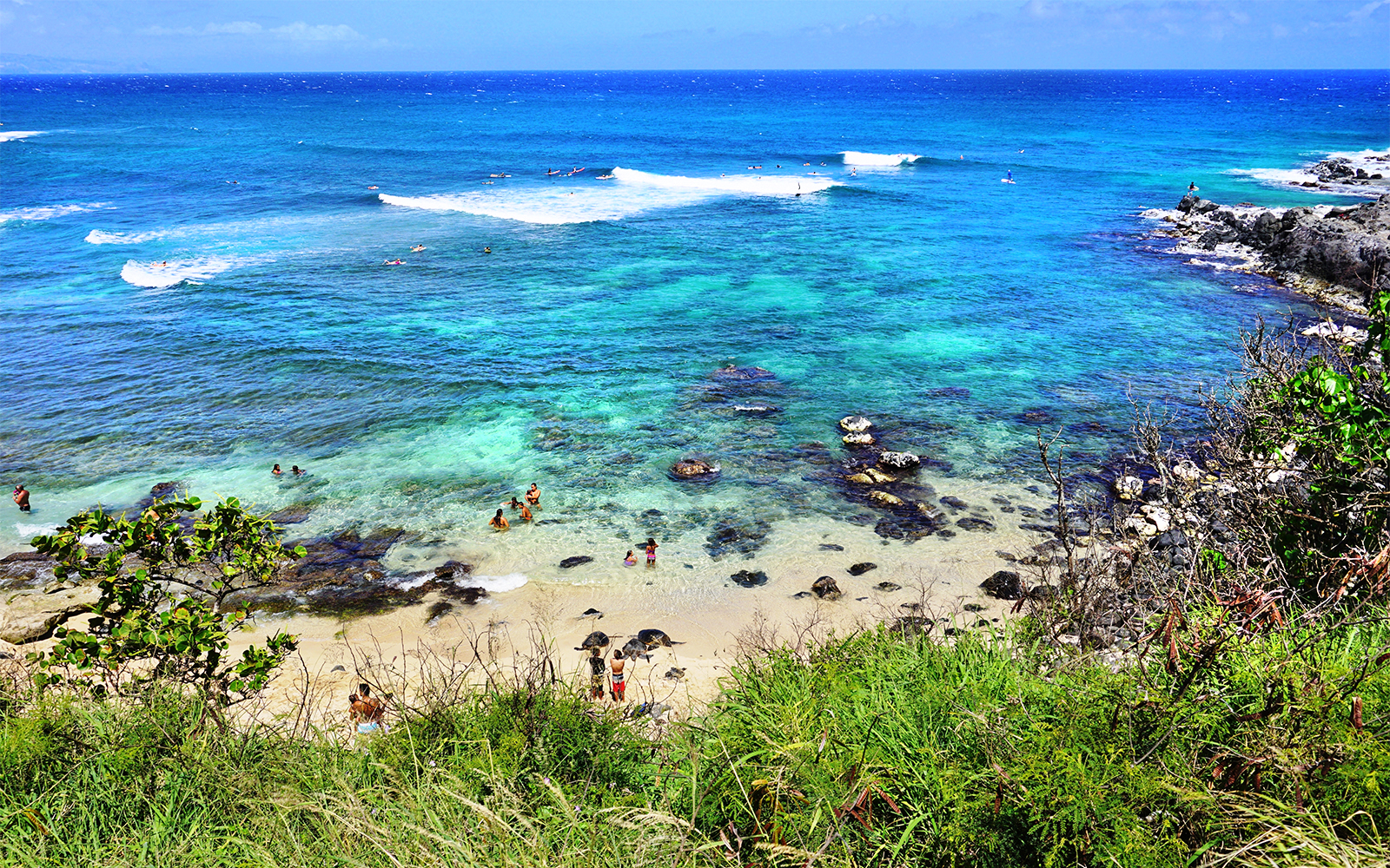 Visitors swimming and relaxing at Hookipa Beach Park, Maui, Hawaii, with clear blue ocean and rocky shore.
