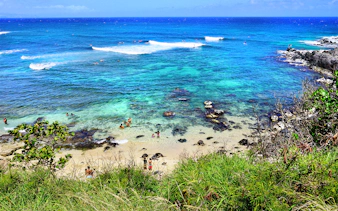 Visitors swimming and relaxing at Hookipa Beach Park, Maui, Hawaii, with clear blue ocean and rocky shore.