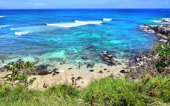 Visitors swimming and relaxing at Hookipa Beach Park, Maui, Hawaii, with clear blue ocean and rocky shore.