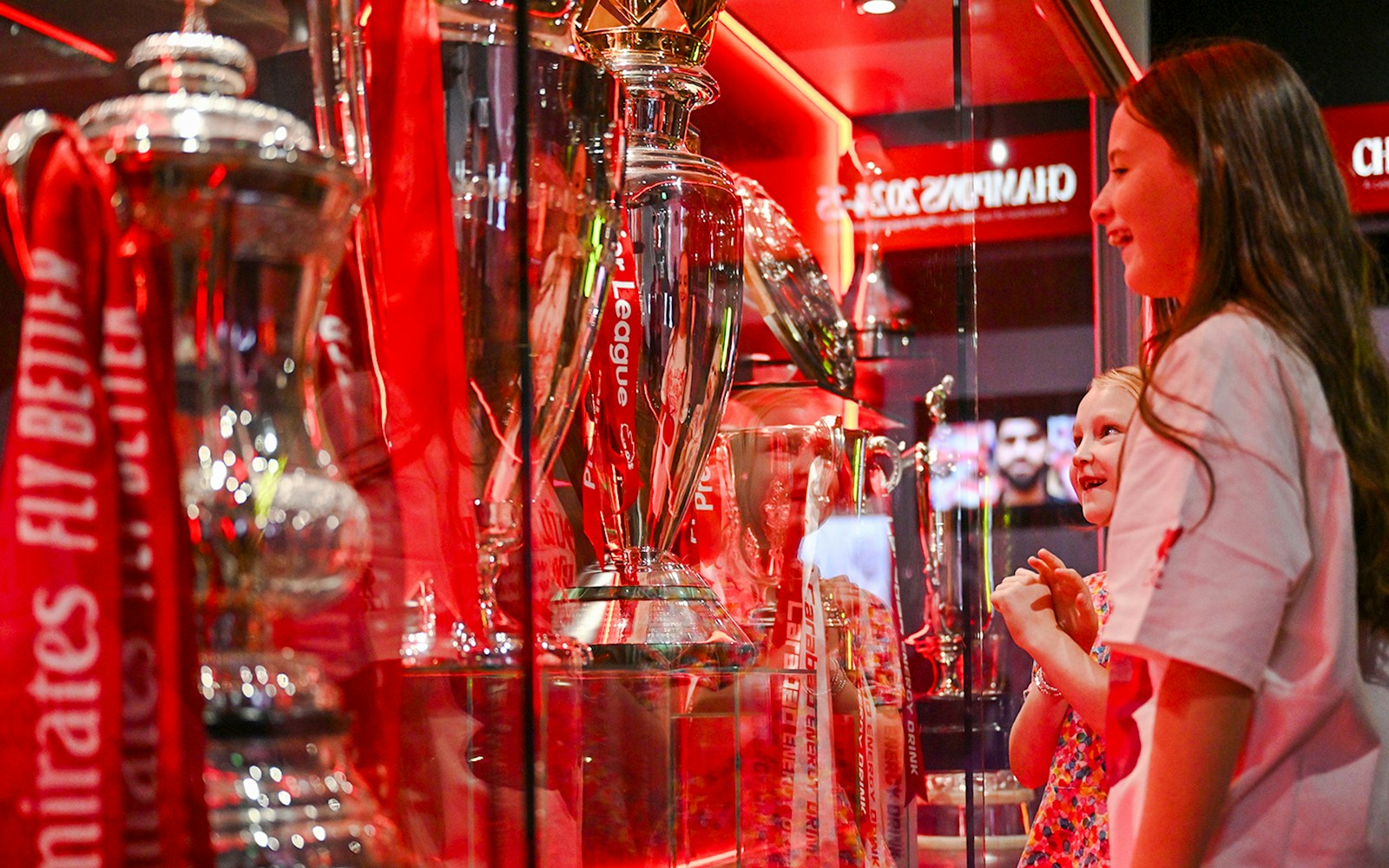 Trophies on display at Liverpool FC Stadium's Anfield trophy cabinet with visitors observing.
