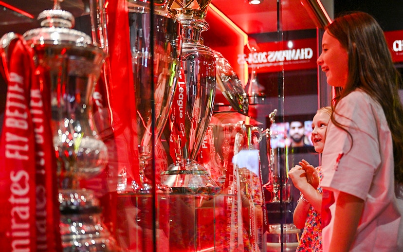 Trophies on display at Liverpool FC Stadium's Anfield trophy cabinet with visitors observing.