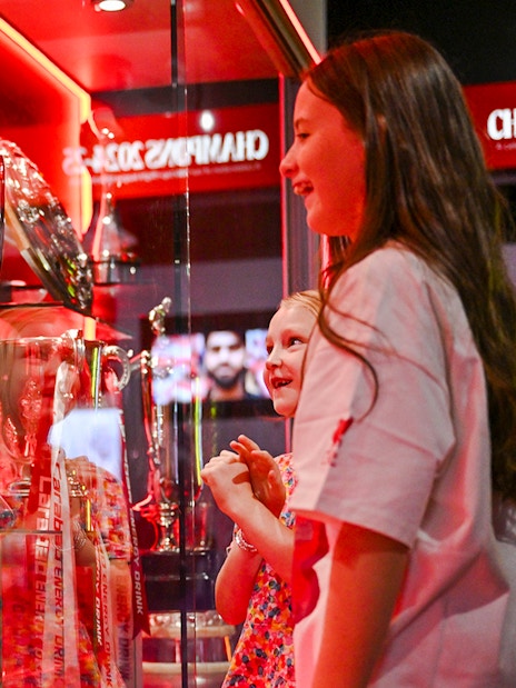 Trophies on display at Liverpool FC Stadium's Anfield trophy cabinet with visitors observing.