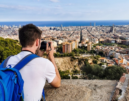 Person photographing Barcelona skyline from Bunkers del Carmel viewpoint.