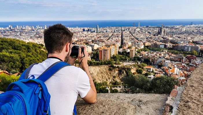 Person photographing Barcelona skyline from Bunkers del Carmel viewpoint.
