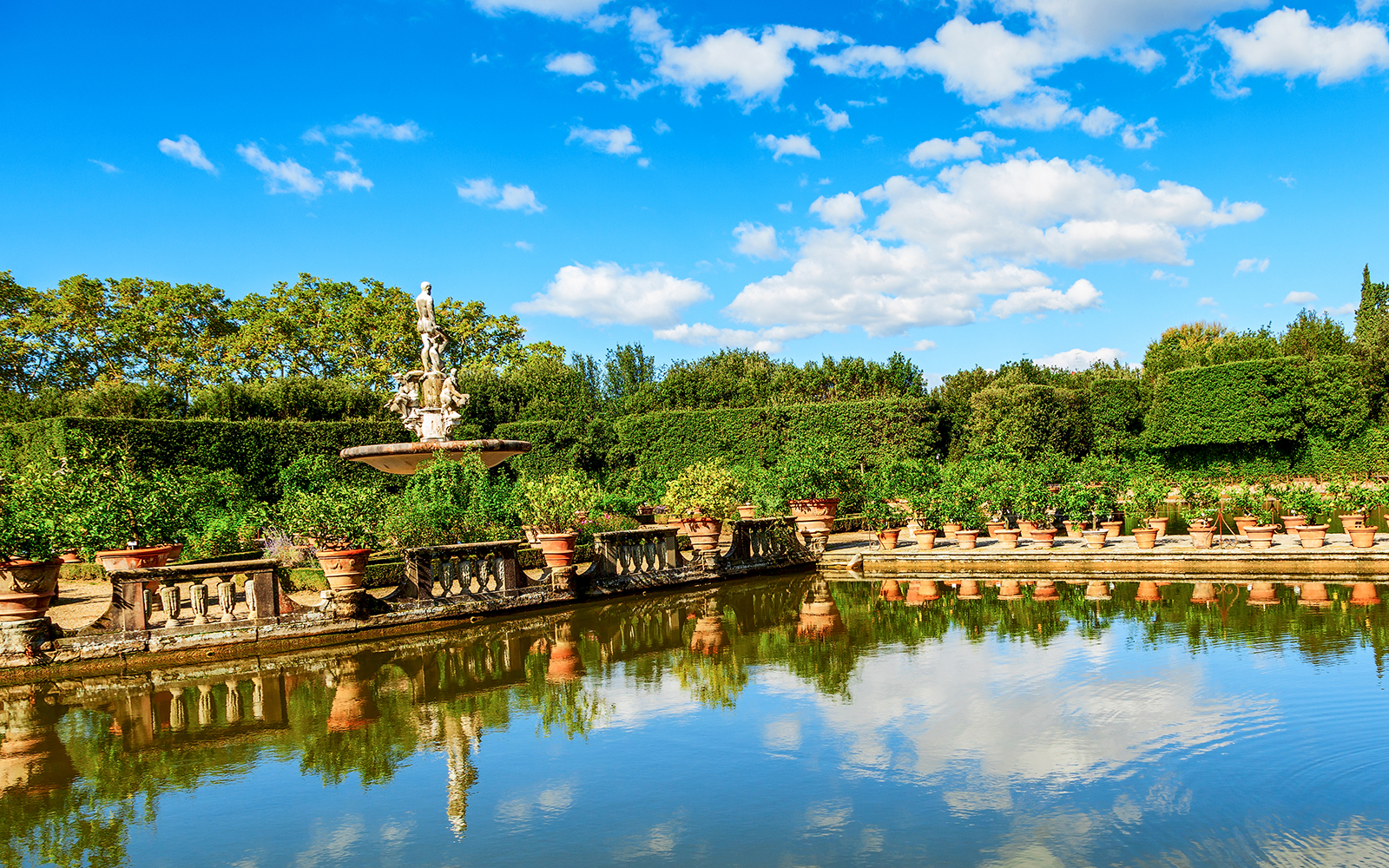 Fountain and statues in the Boboli Gardens, Florence, with surrounding greenery and reflection in water.