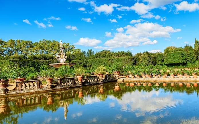 Fountain and statues in the Boboli Gardens, Florence, with surrounding greenery and reflection in water.