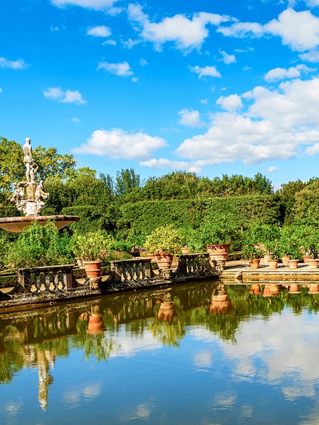 Fountain and statues in the Boboli Gardens, Florence, with surrounding greenery and reflection in water.