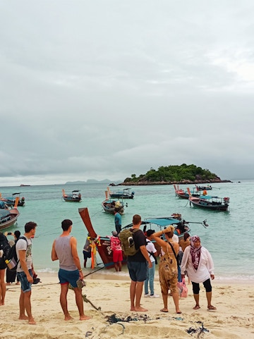 Tourists boarding long-tail boats on a sandy beach in Thailand.