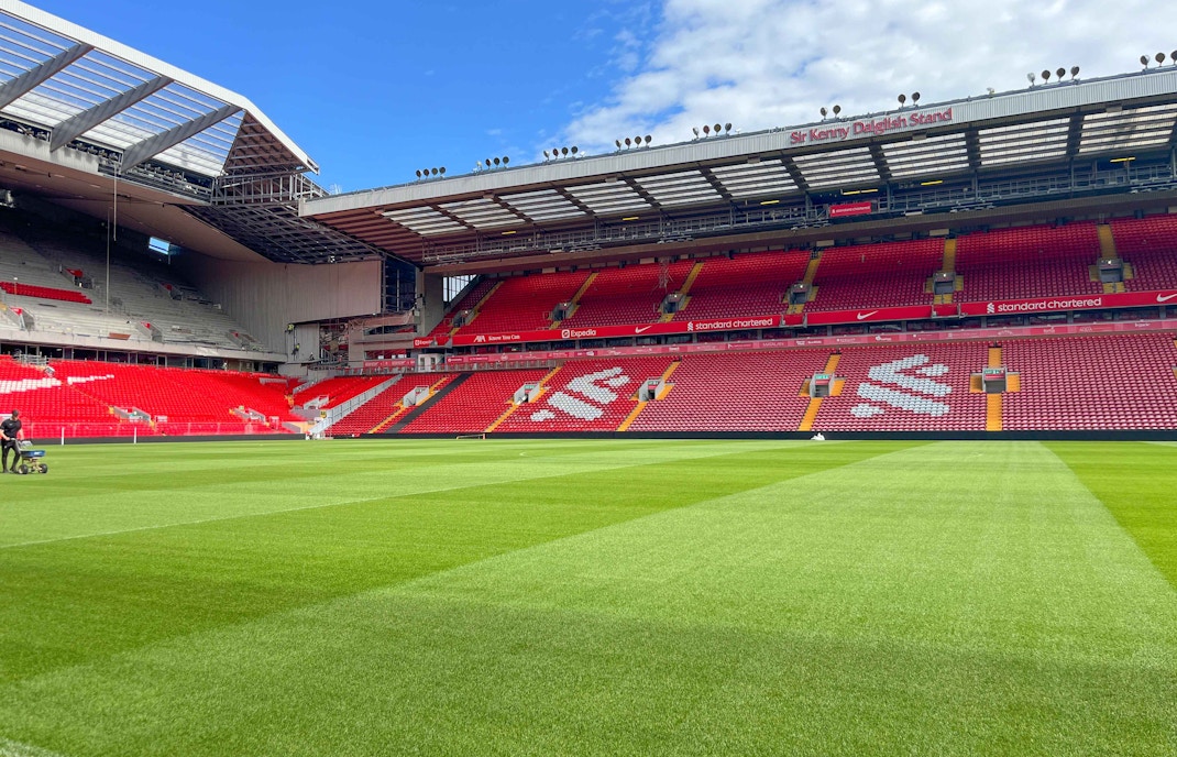 Liverpool FC stadium with empty red seats and green pitch.