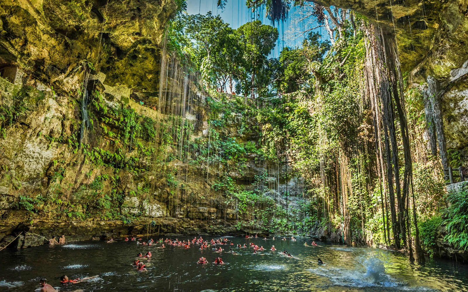 Swimmers enjoying Cenote Ik Kil, a natural sinkhole surrounded by lush vegetation in Yucatan, Mexico.