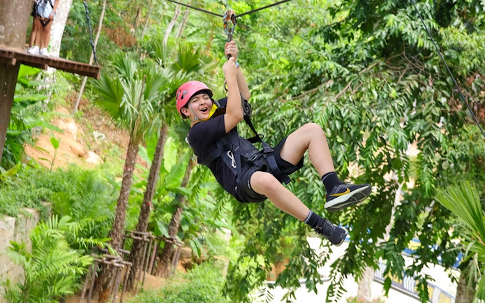 Person ziplining through lush forest at Hanuman World, Thailand.