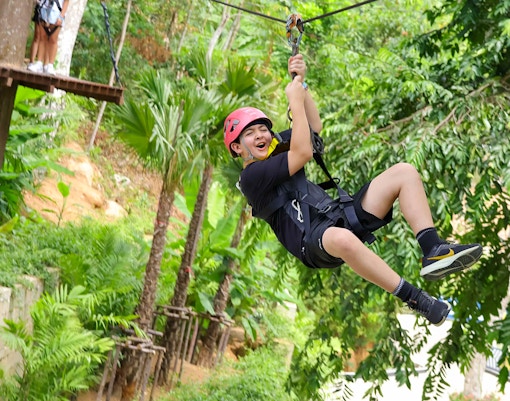 Person ziplining through lush forest at Hanuman World, Thailand.