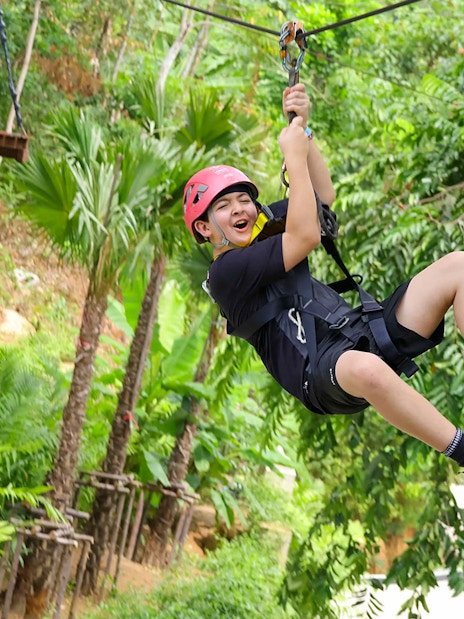 Person ziplining through lush forest at Hanuman World, Thailand.