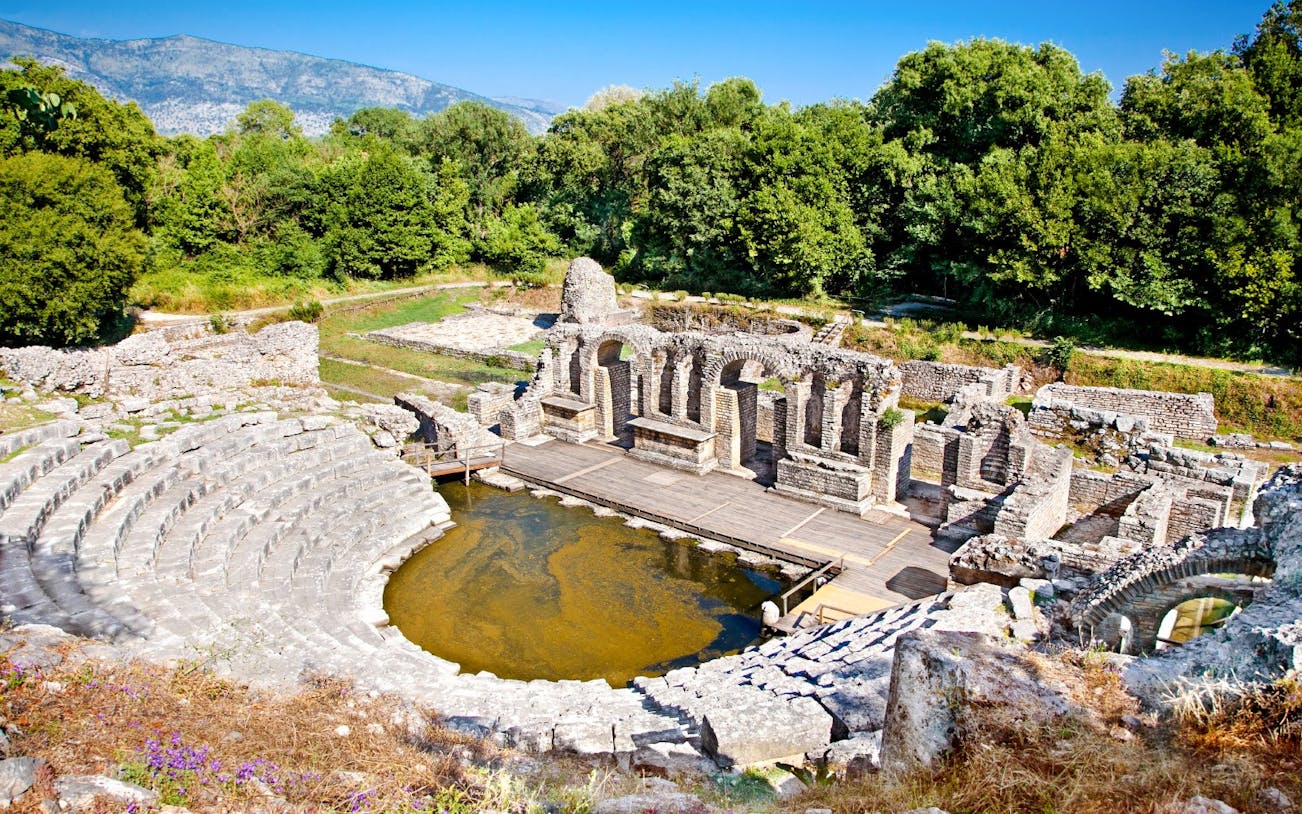 Amphitheater ruins at the ancient Baptistery in Butrint, Albania, surrounded by lush greenery.