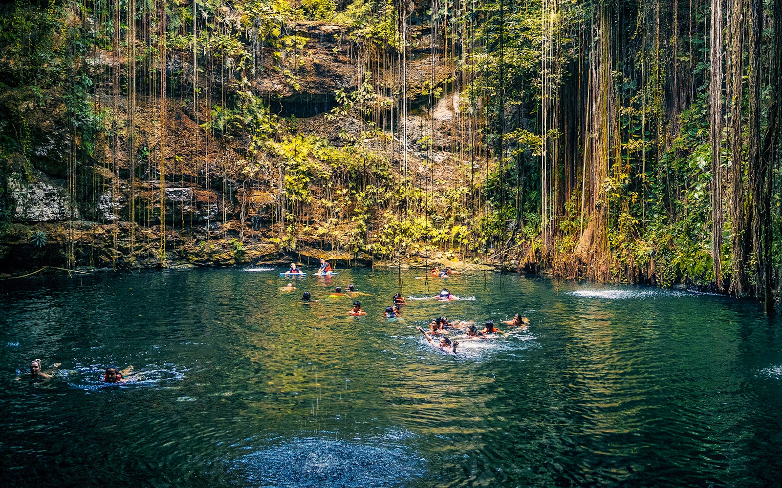 People swimming in a cenote surrounded by lush vegetation in Chichen Itza, Mexico.