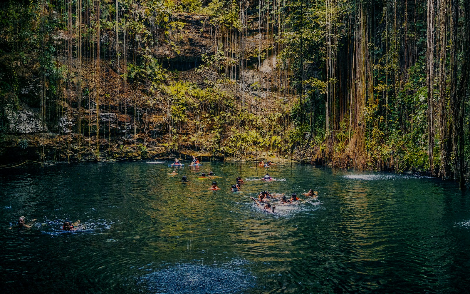 People swimming in a cenote surrounded by lush vegetation in Chichen Itza, Mexico.