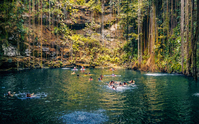 People swimming in a cenote surrounded by lush vegetation in Chichen Itza, Mexico.