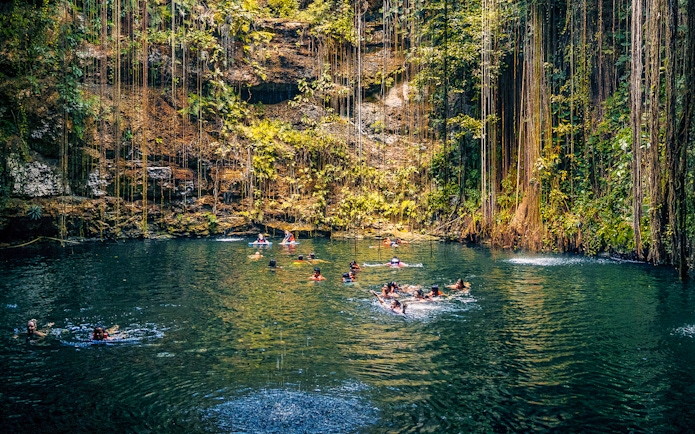 People swimming in a cenote surrounded by lush vegetation in Chichen Itza, Mexico.