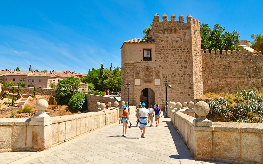 Visitors walking on San Martin Bridge towards medieval gate, Toledo.