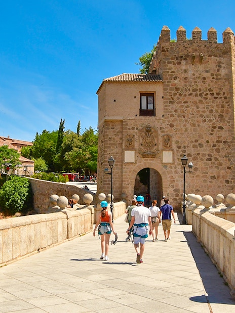 Visitors walking on San Martin Bridge towards medieval gate, Toledo.