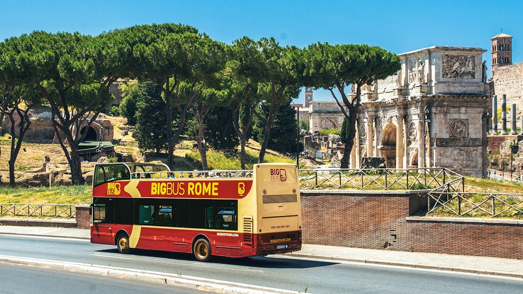 Big Bus Rome tour passing by the Arch of Constantine with tourists on board.