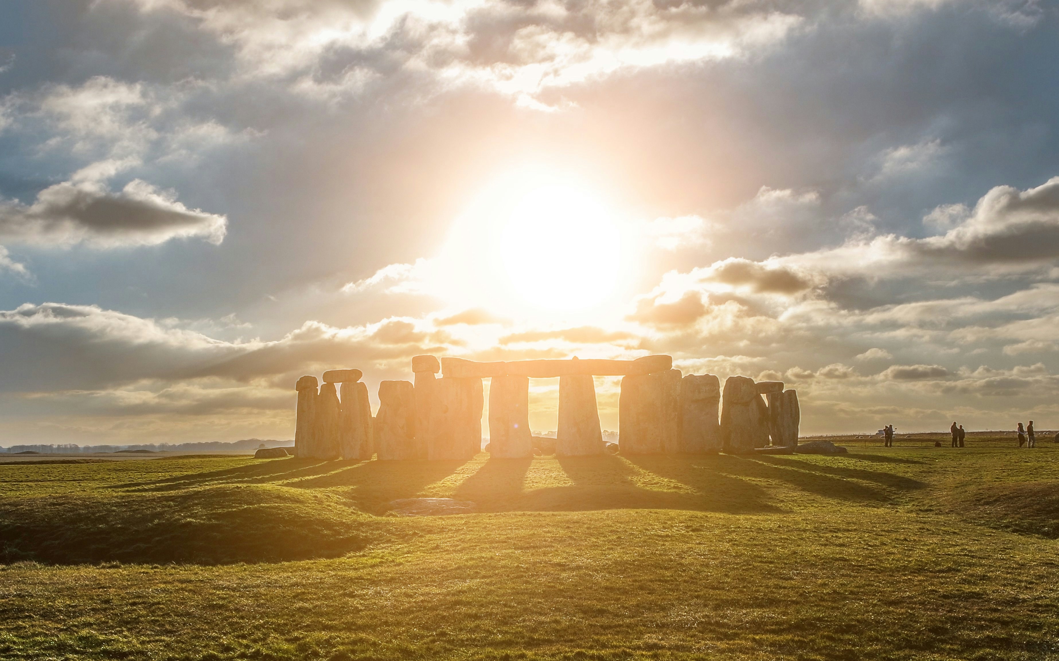 Stonehenge at sunset with sun rays casting shadows on the grass.
