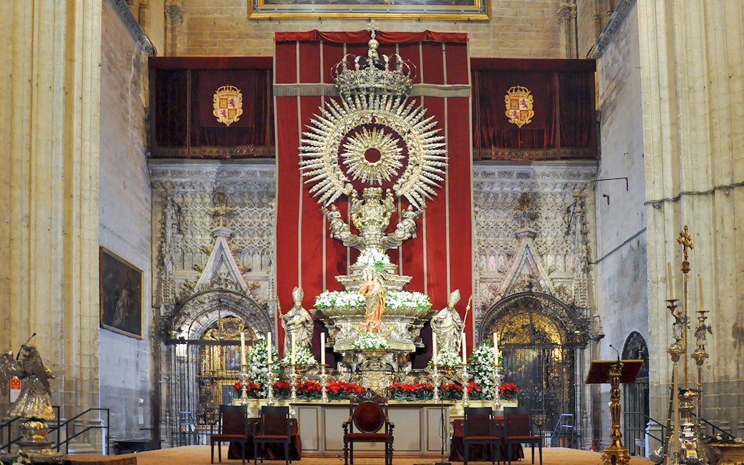 Altar of Seville Cathedral adorned with ornate sculptures and floral arrangements.