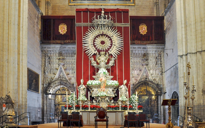 Altar of Seville Cathedral adorned with ornate sculptures and floral arrangements.