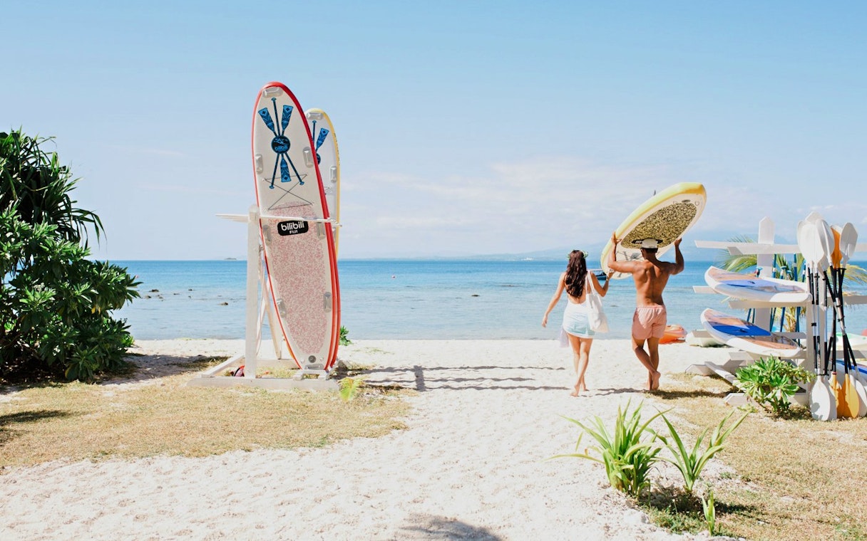 Couple carrying paddleboard towards ocean at Malamala Beach Club, Fiji.