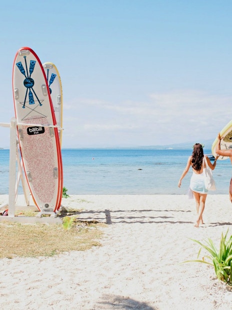 Couple carrying paddleboard towards ocean at Malamala Beach Club, Fiji.