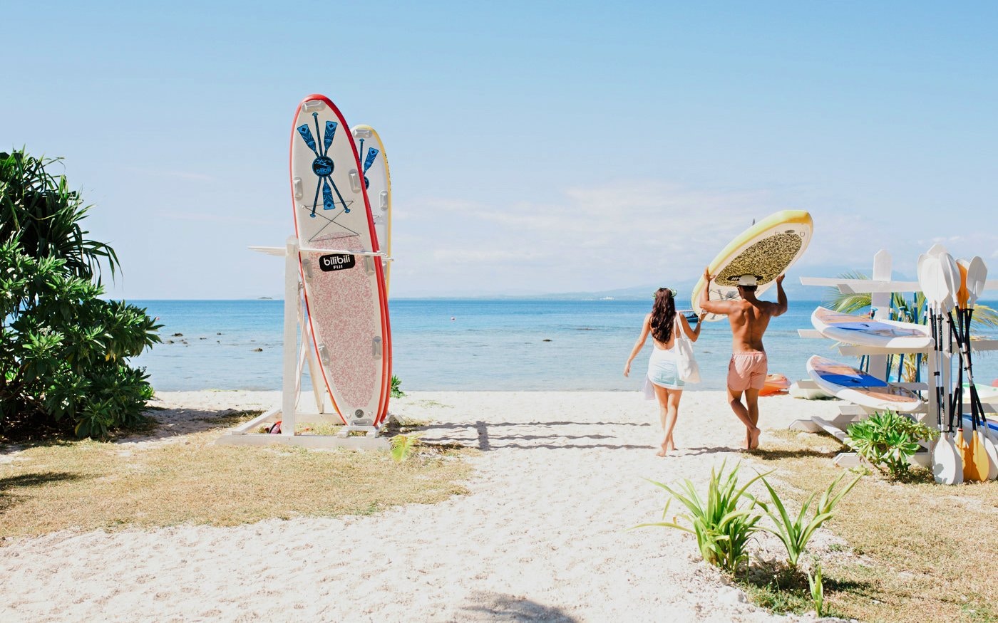 Couple carrying paddleboard towards ocean at Malamala Beach Club, Fiji.