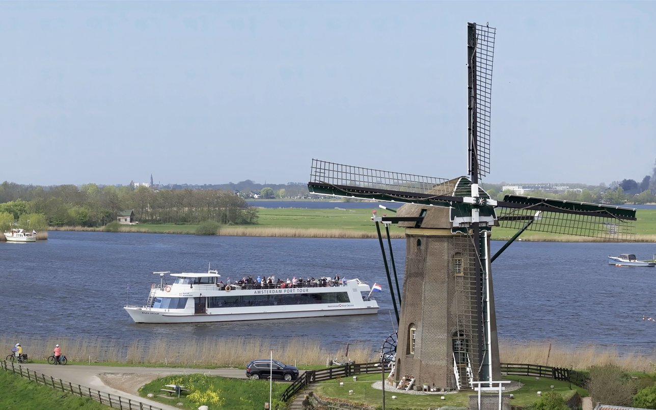 Cruise boat passing by a windmill on a river at Keukenhof, Netherlands.