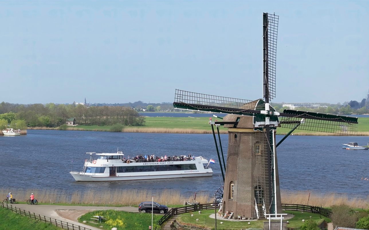 Cruise boat passing by a windmill on a river at Keukenhof, Netherlands.