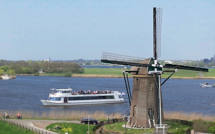 Cruise boat passing by a windmill on a river at Keukenhof, Netherlands.