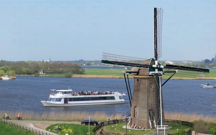 Cruise boat passing by a windmill on a river at Keukenhof, Netherlands.