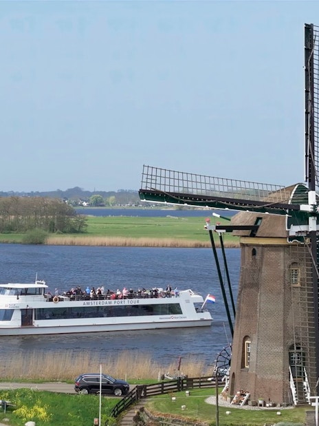 Cruise boat passing by a windmill on a river at Keukenhof, Netherlands.