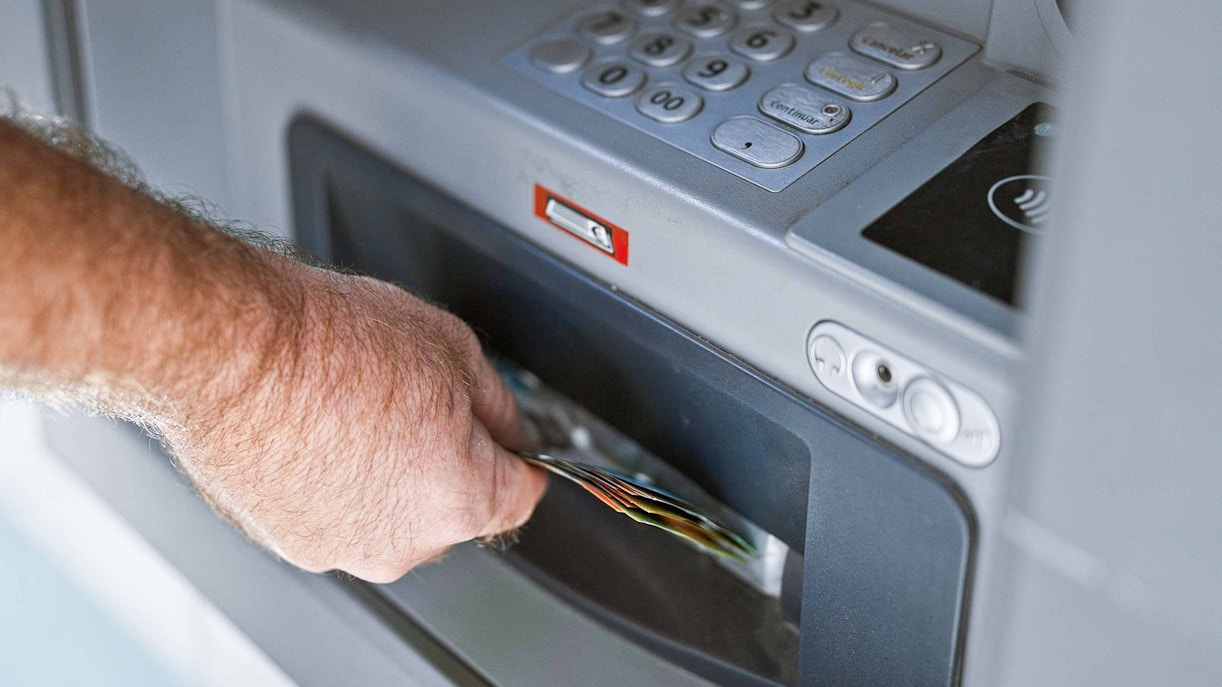 Hand retrieving cash from an ATM machine.