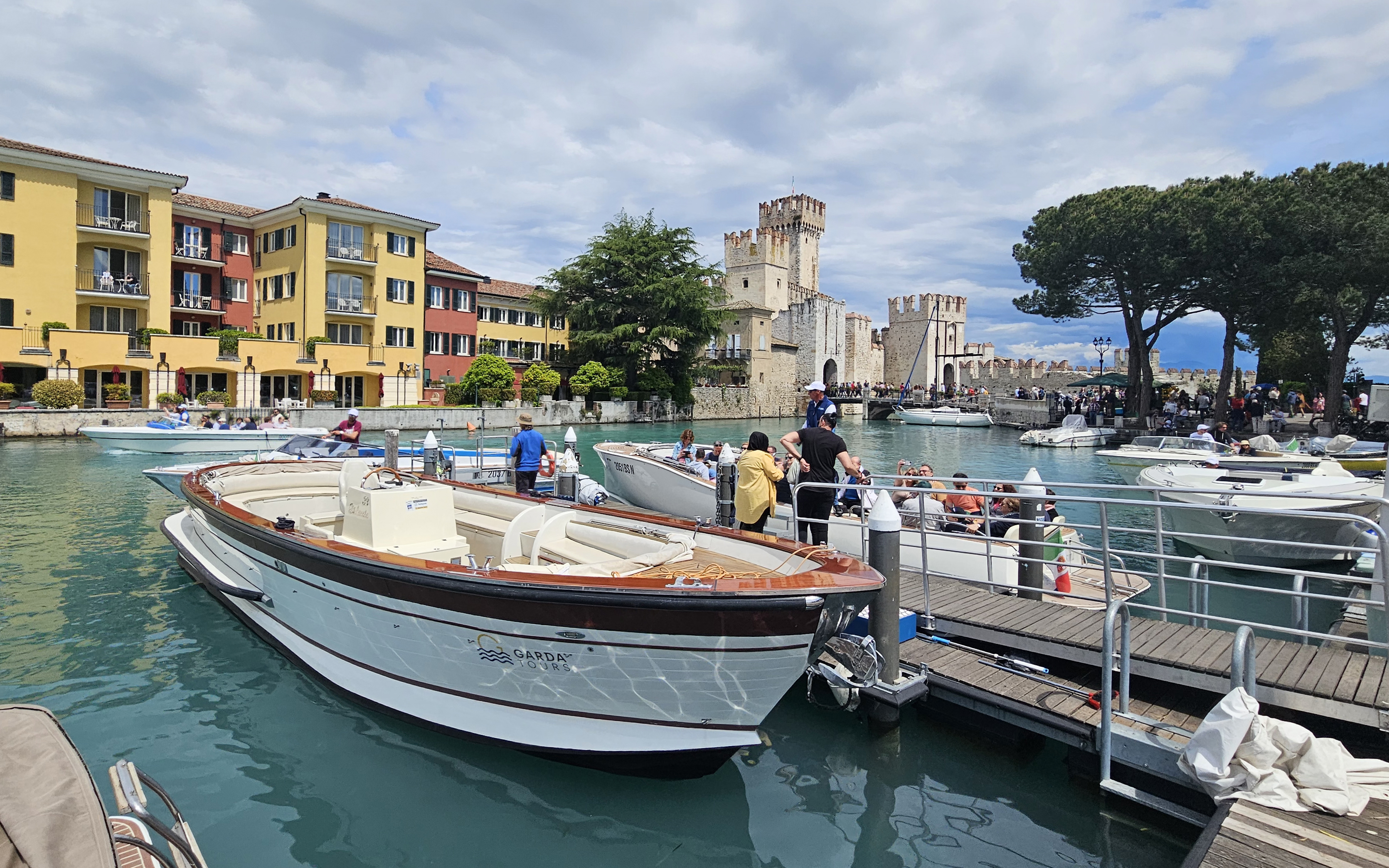 People boarding a boat for a private tour around Sirmione, with Scaliger Castle in the background.