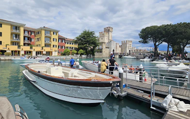 People boarding a boat for a private tour around Sirmione, with Scaliger Castle in the background.