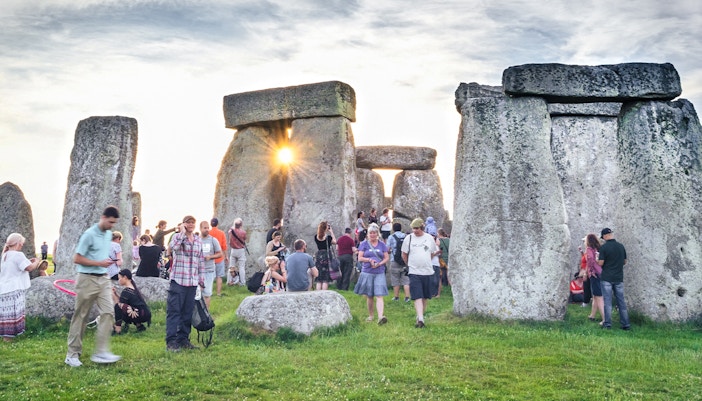 Tourists exploring the inner circle of Stonehenge at sunset.