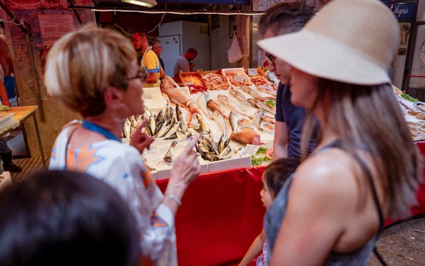 Market tour group exploring fresh seafood stall in Palermo.