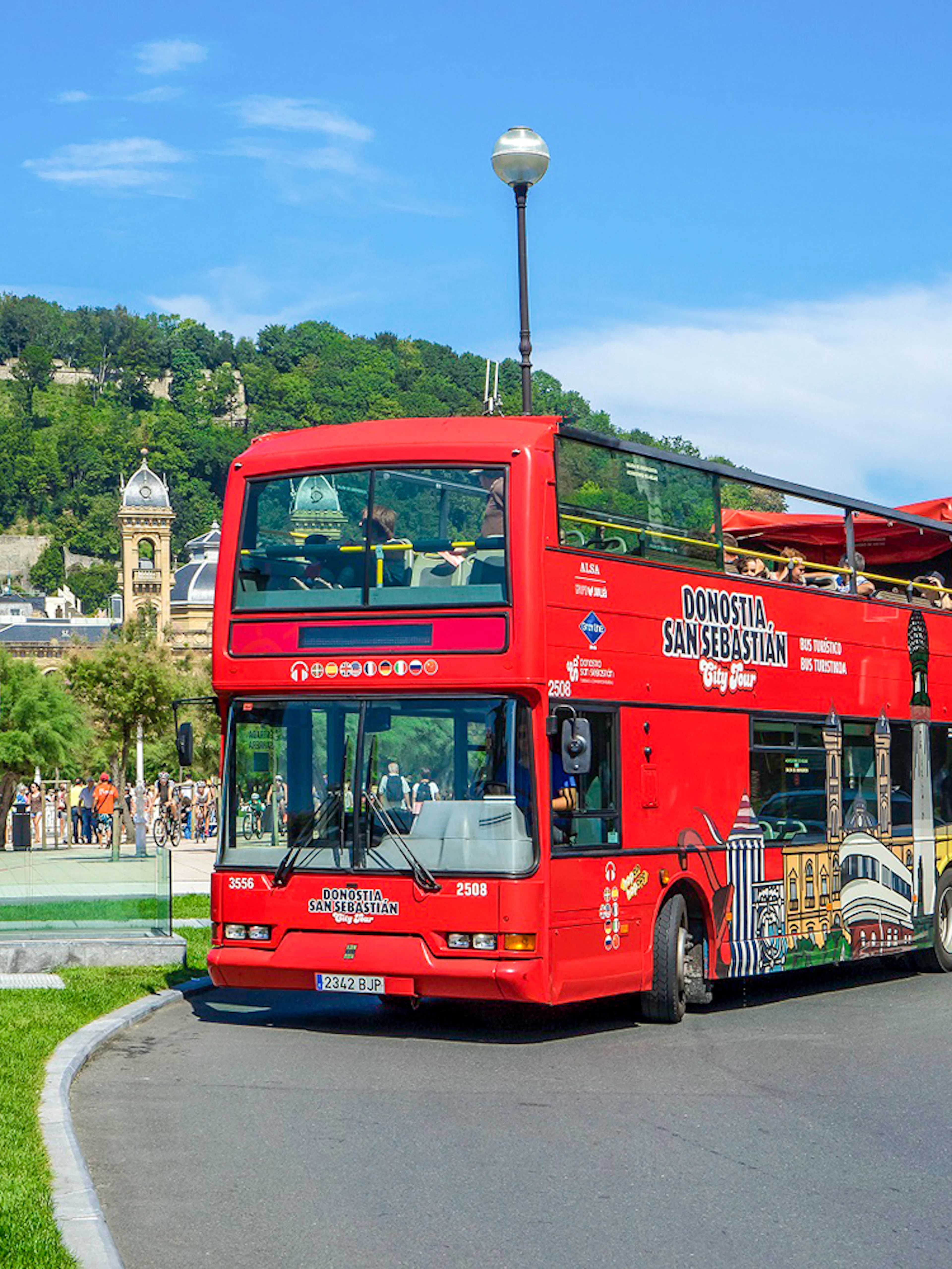 Red double-decker tour bus in San Sebastian with Monte Urgull in the background.
