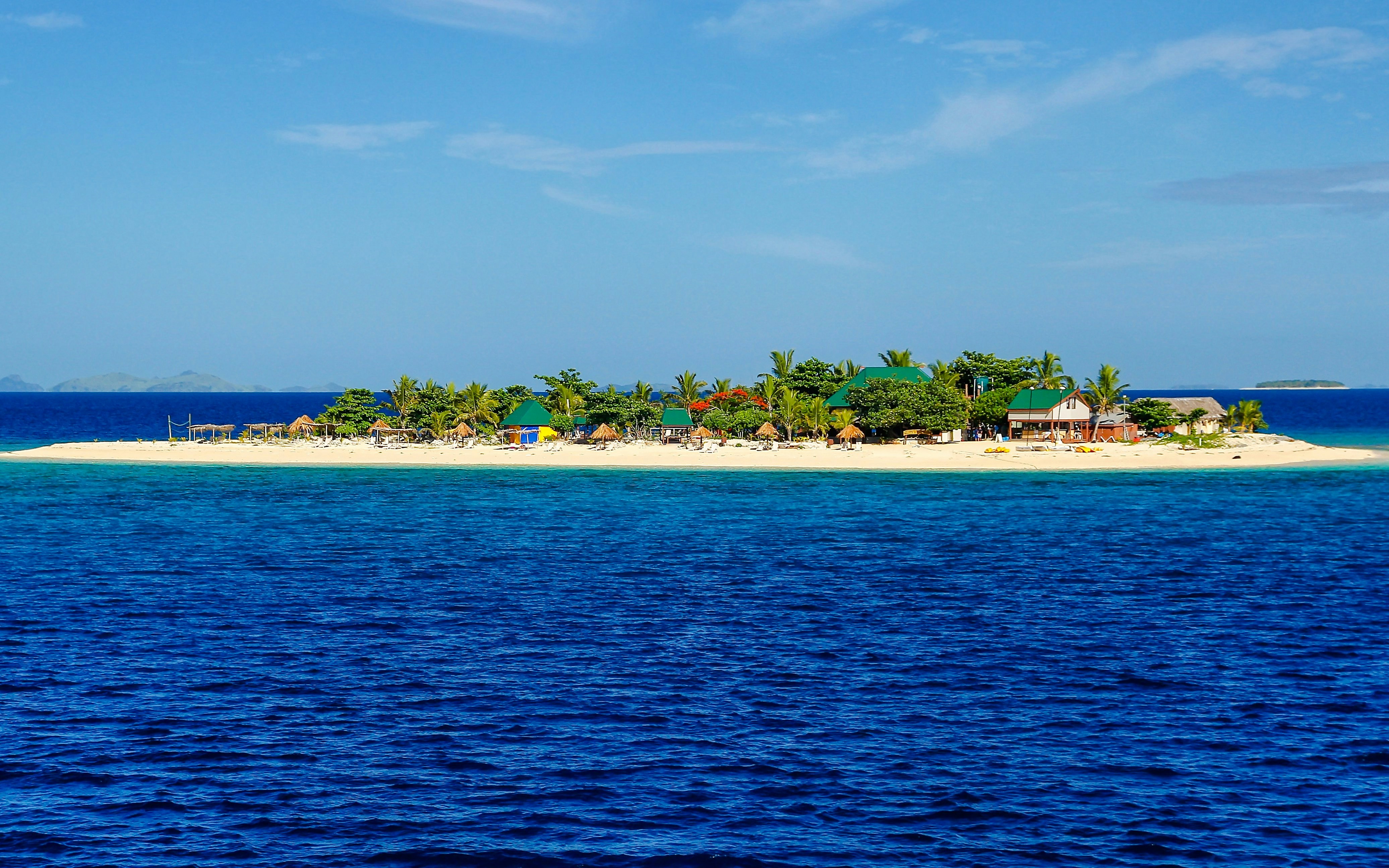 Small South Sea Island with palm trees and huts in Mamanuca Island group, Fiji.