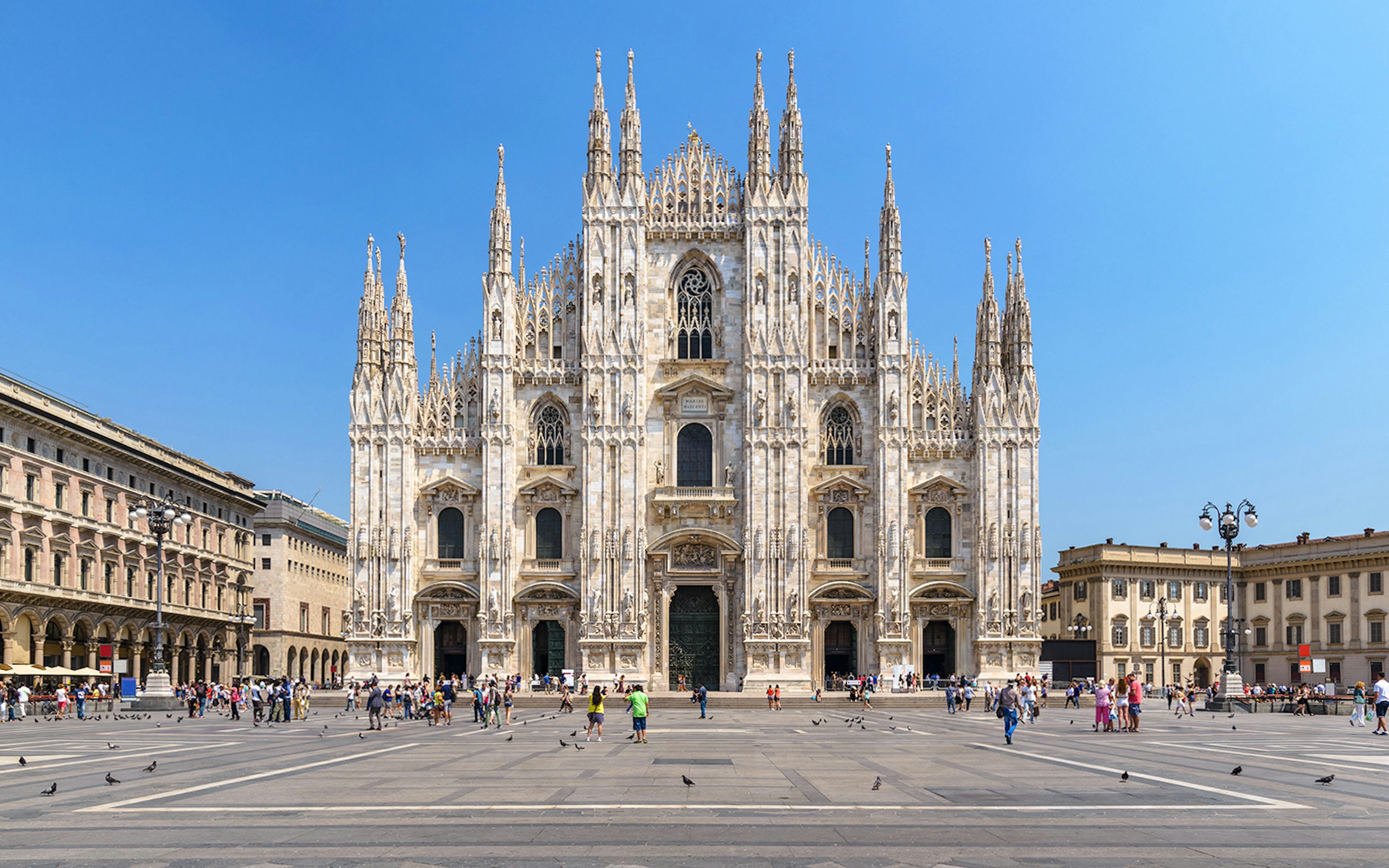 Duomo Milan Cathedral facade with tourists exploring architectural details.