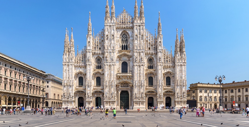 Duomo Milan Cathedral facade with tourists exploring architectural details.
