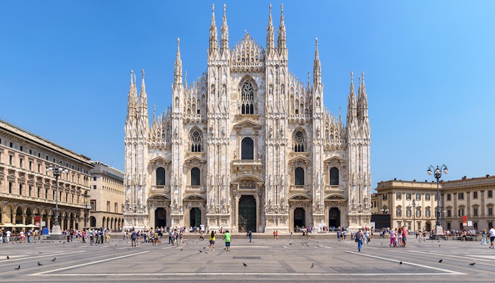 Duomo Milan Cathedral facade with tourists on guided tour, showcasing architectural details.
