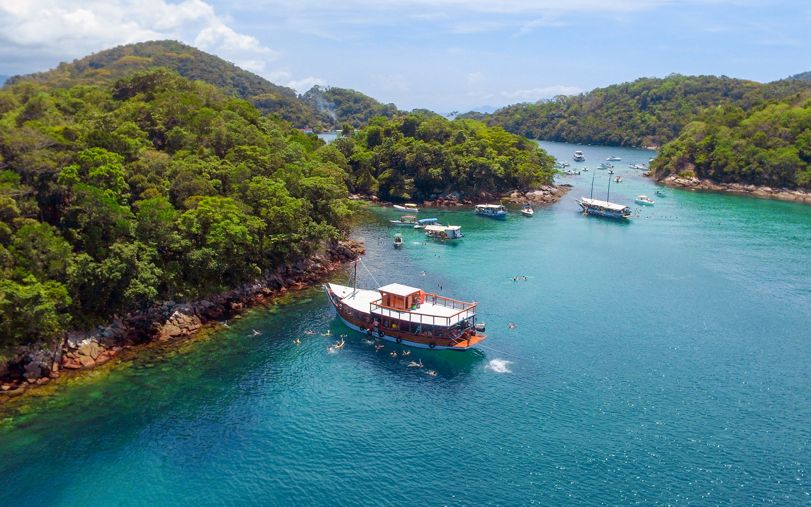 Boat navigating clear waters surrounded by lush islands in Ilha Grande, Brazil.