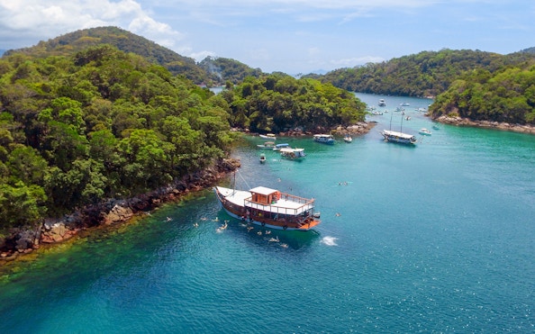 Boat navigating clear waters surrounded by lush islands in Ilha Grande, Brazil.