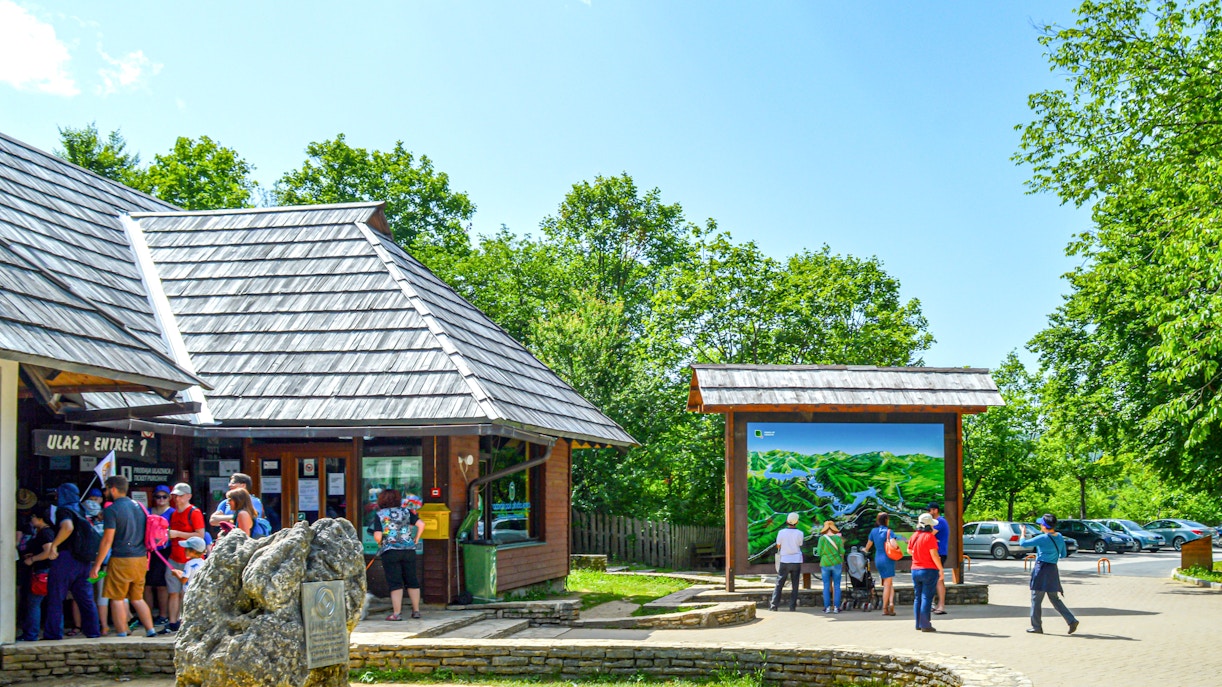 Entrance to Plitvice Lakes National Park with visitors and a large map display.